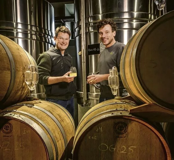 Franck Bonville team members tasting champagne inside the winery, surrounded by oak barrels and stainless steel fermentation tanks.