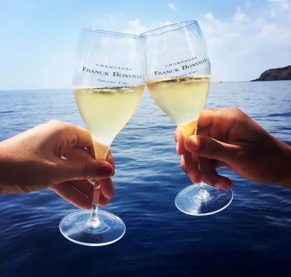 Two glasses of Franck Bonville Grand Cru Champagne raised in a celebratory toast overlooking the ocean, capturing a premium champagne experience.