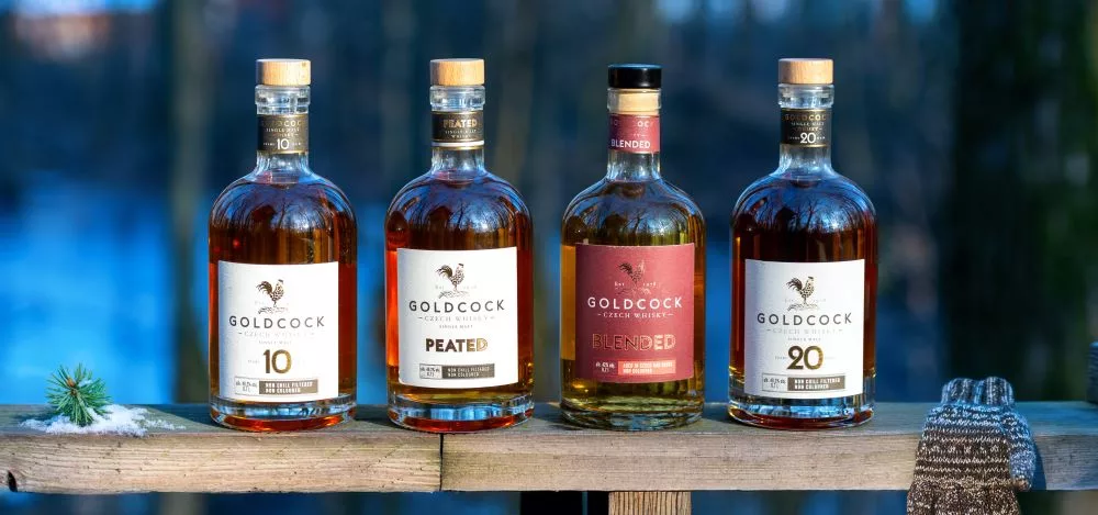 Collection of Gold Cock Czech whisky bottles featuring 10 Year, Peated, Blended and 20 Year expressions displayed outdoors.