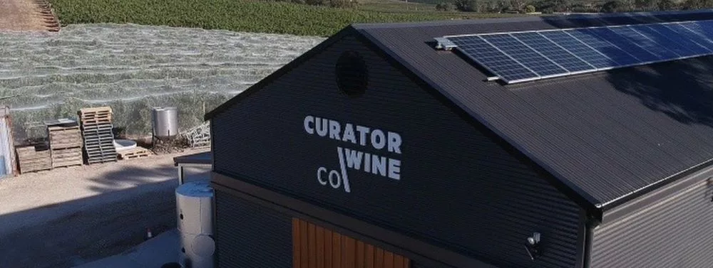 Exterior of the Curator Wine Co. winery building in Barossa Valley with vineyard views and rooftop solar panels, representing sustainable Australian winemaking.