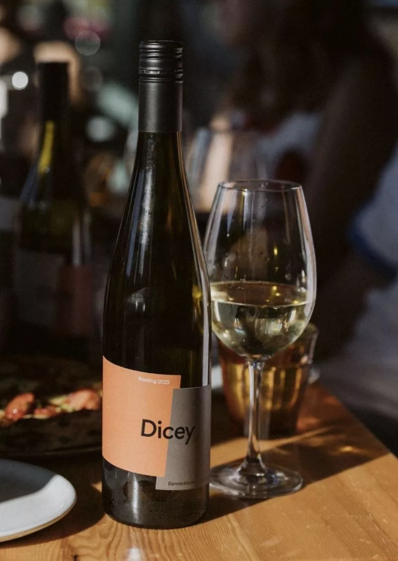 Bottle of Dicey Riesling beside a glass of white wine, ready to enjoy in a relaxed dining setting.